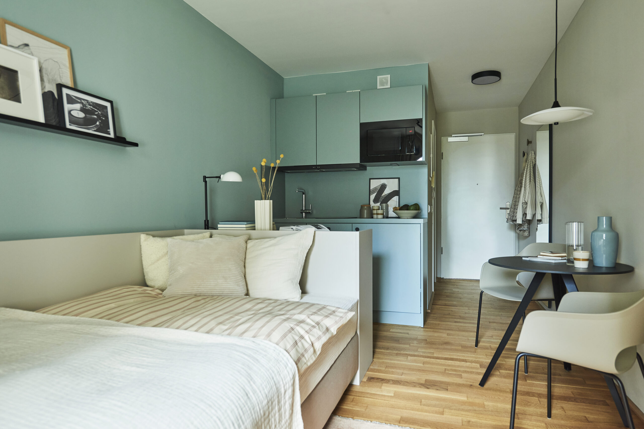 Zu sehen ist ein Apartment im Little East Frankfurt mit Bett, einer Küchenzeile sowie einem kleinen Tisch mit zwei Stühlen.