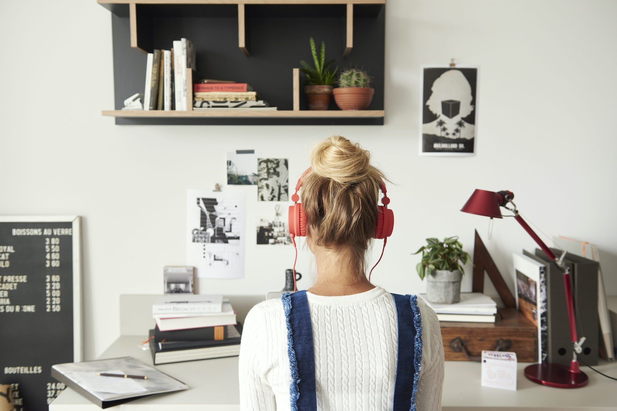 Junge Frau sitzt mit Kopfhörern an einem weißen Schreibtisch