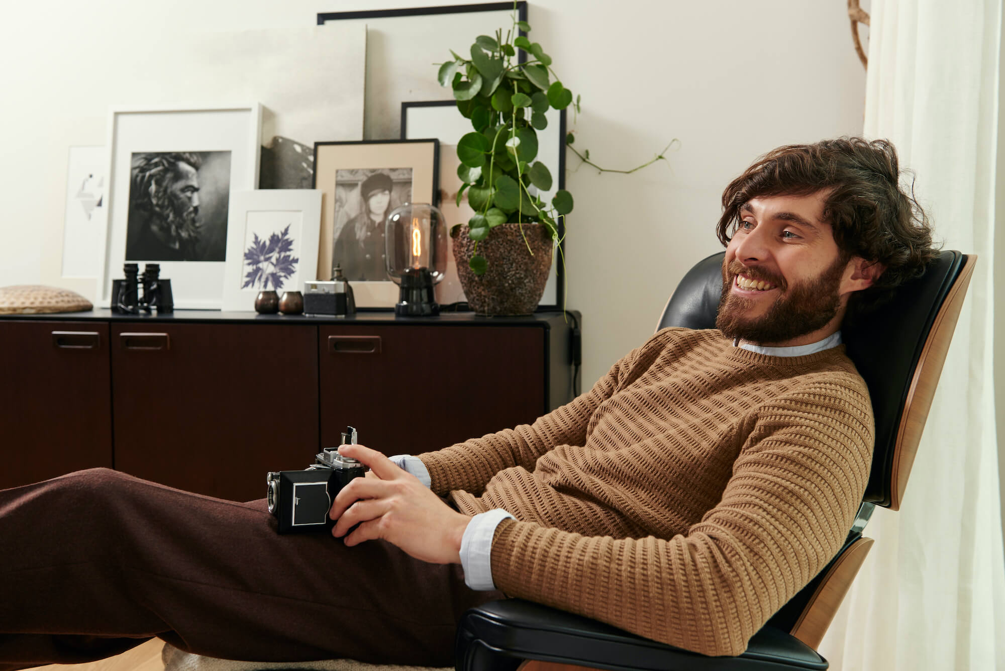 Mann sitzt auf Couch-Stuhl mit einer Retro-Kamera in der Hand und lacht