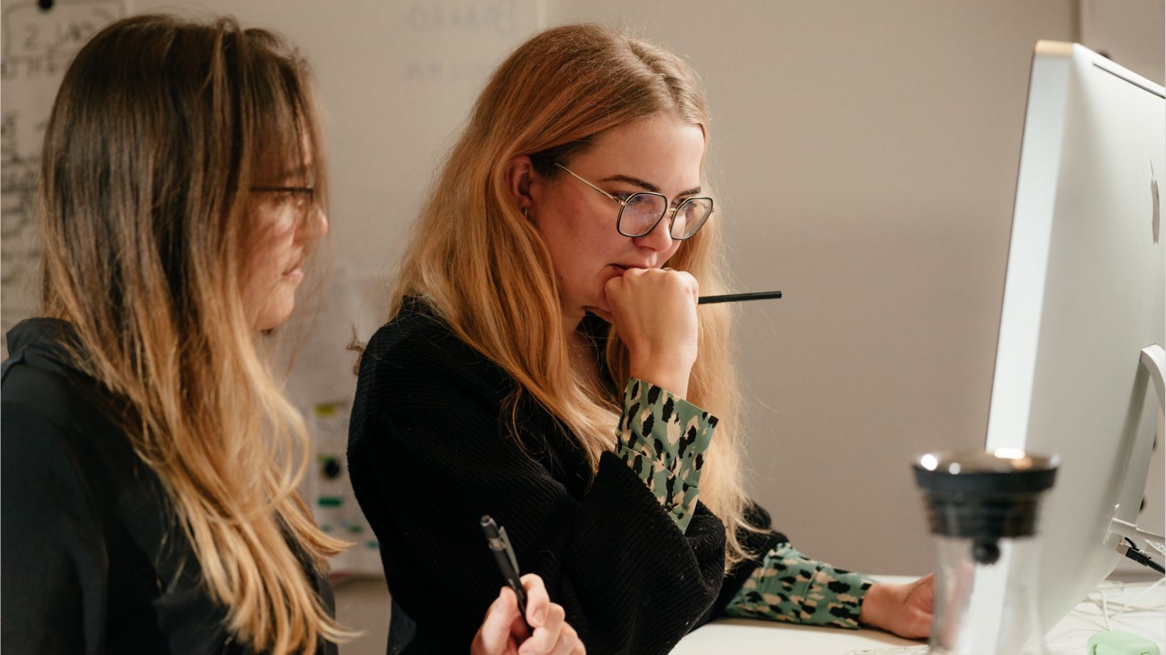 Zwei Studentinnen arbeiten konzentriert mit Stift und Notizen am Bildschirm