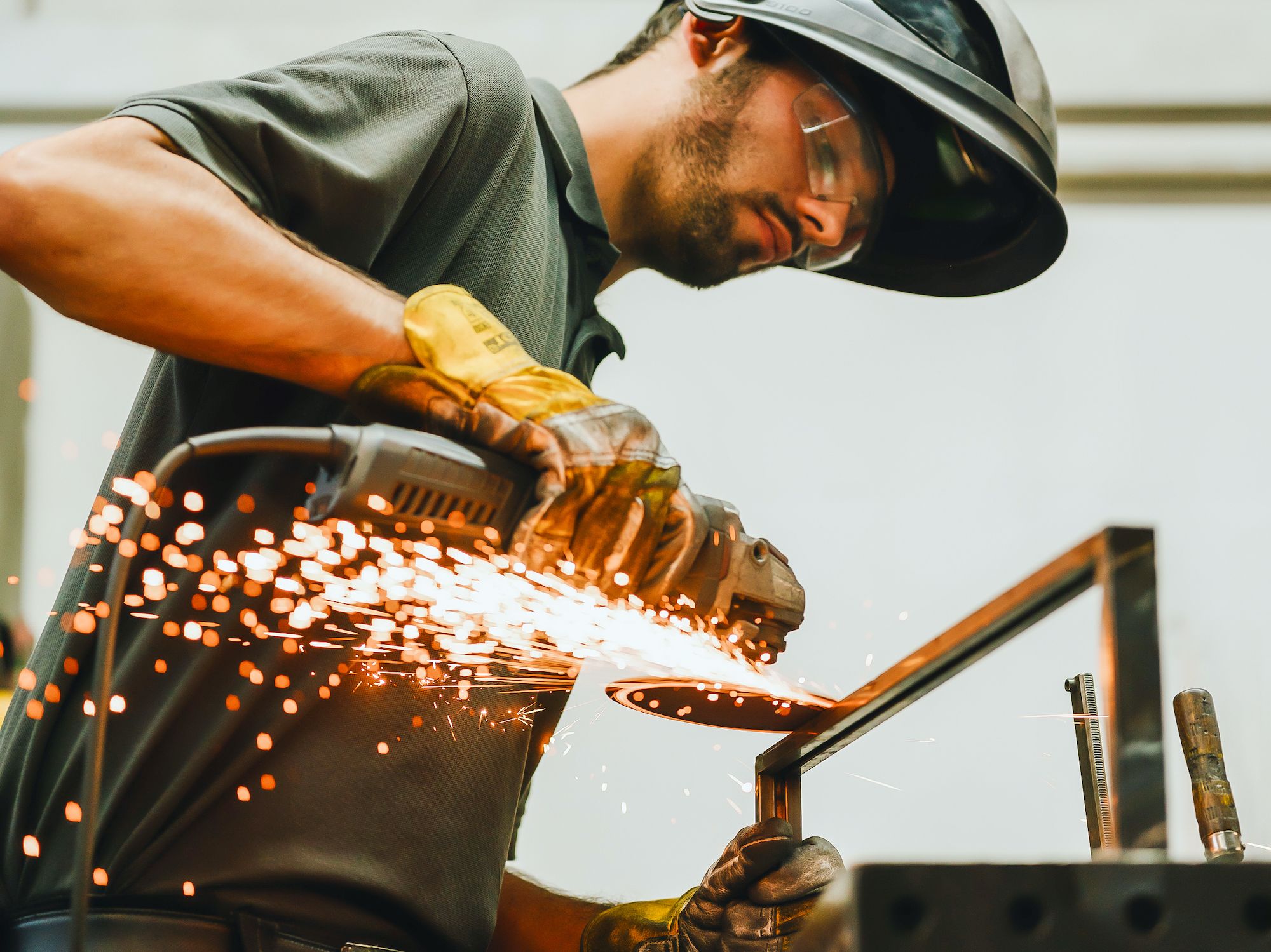 Handwerker mit Schutzbrille und Helm trennt Metall mit Winkelschleifer, Funken fliegen