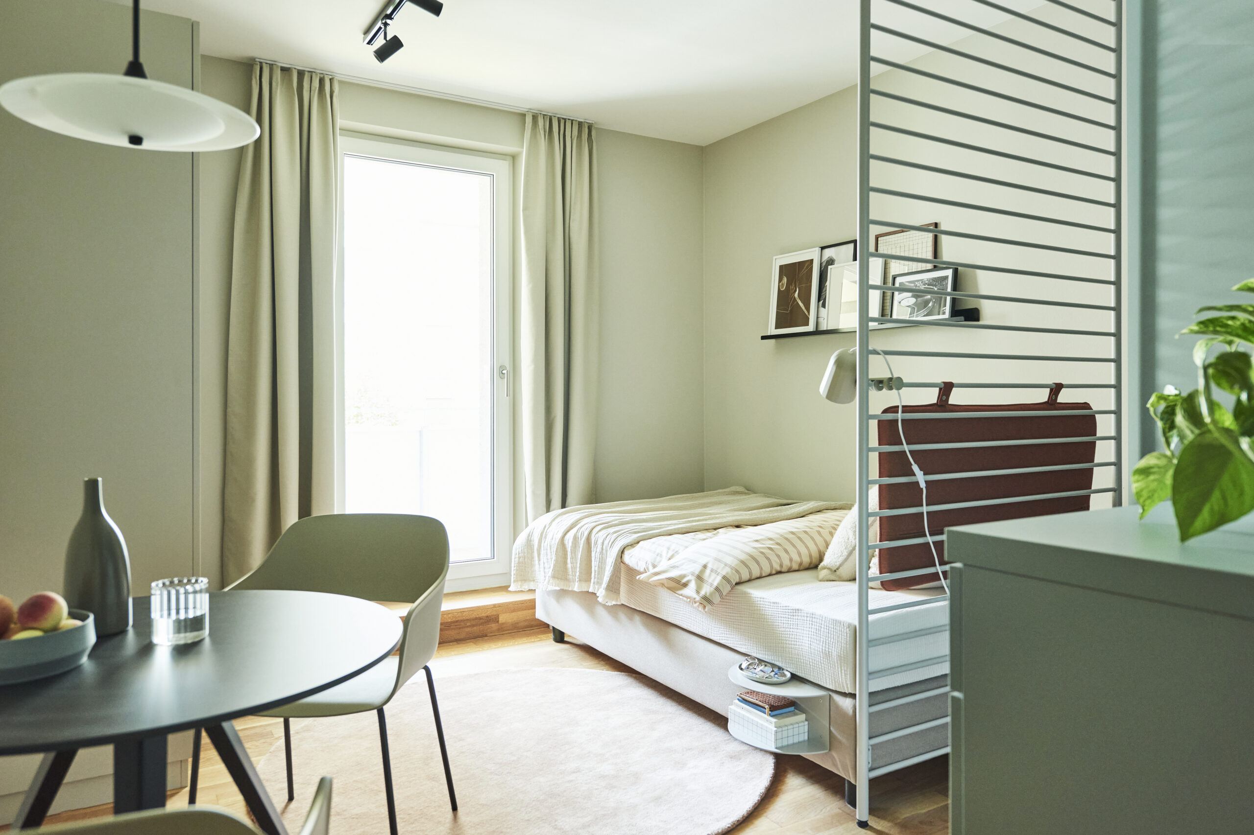 Zu sehen ist ein Bett sowie ein Tisch mit Stuhl in einem Little East Apartment.