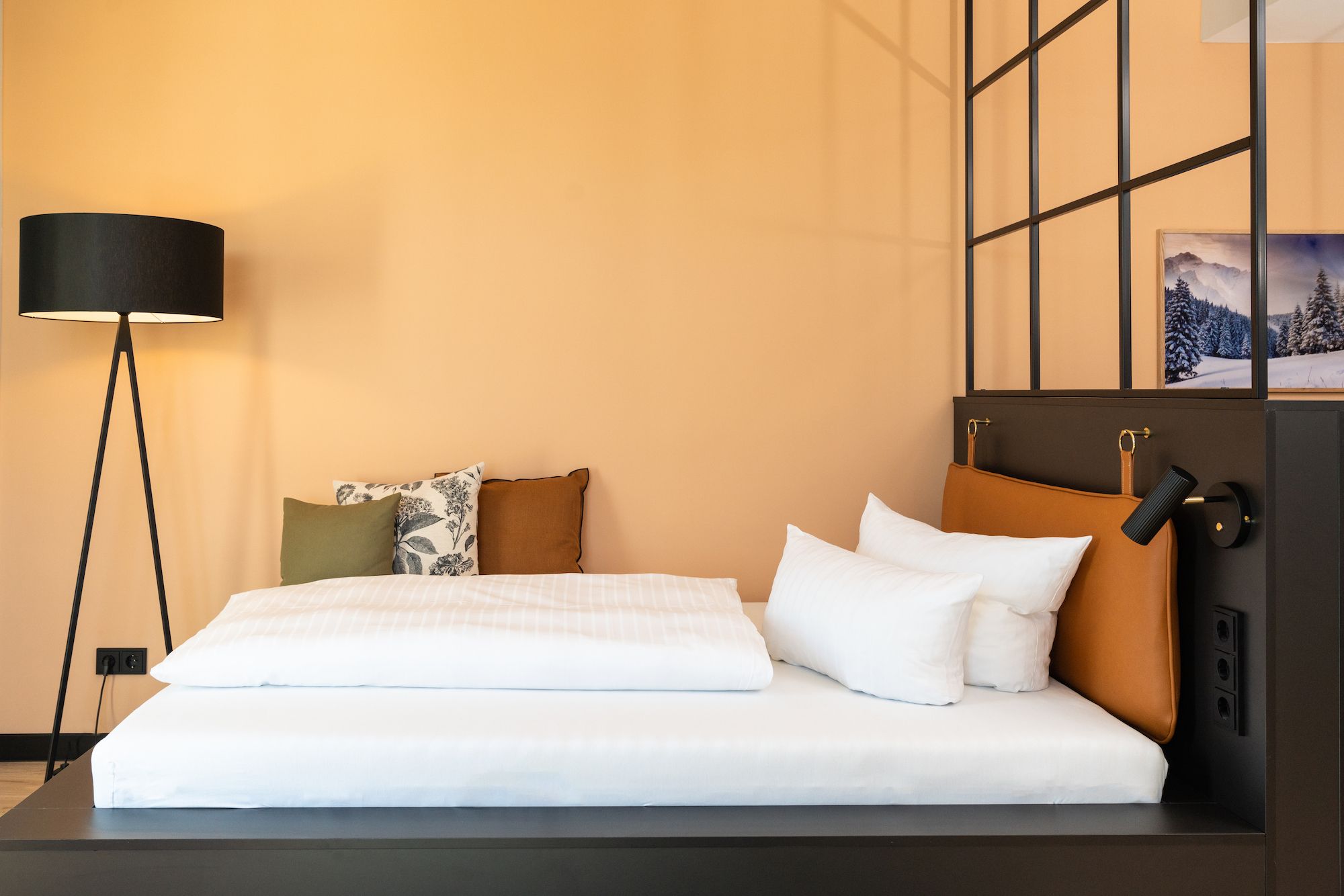 Schlafbereich mit Lederkopfteil, Stehleuchte und apricotfarbener Wand hinter dem Bett