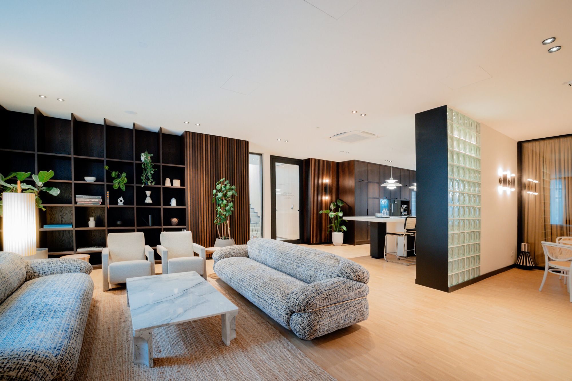 Offene Lounge mit Sofas, Regalwand, Pflanzen und angrenzendem Coworking-Bereich