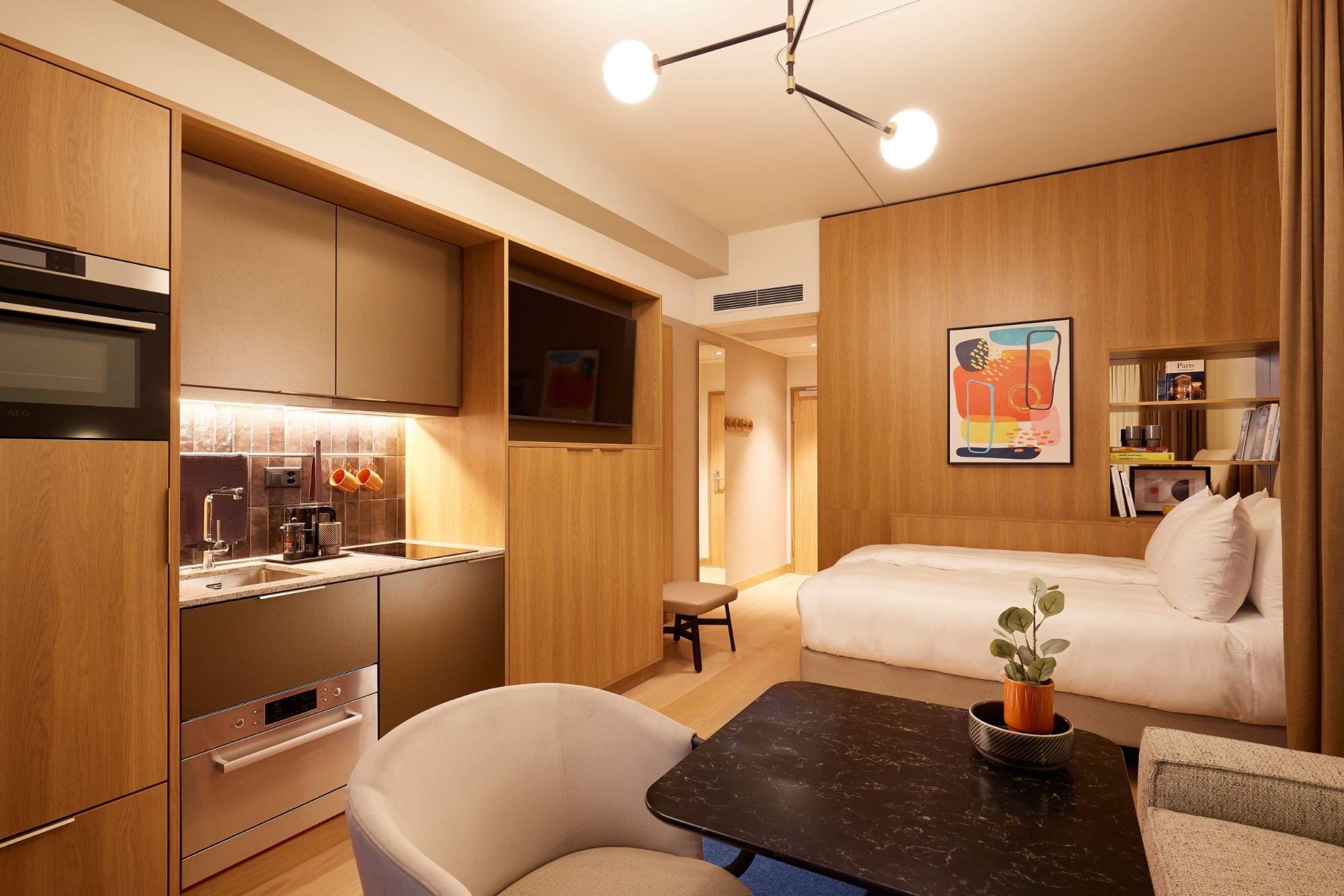 Serviced-Apartment-Zimmer mit Küchenzeile, Bett und Esstisch.