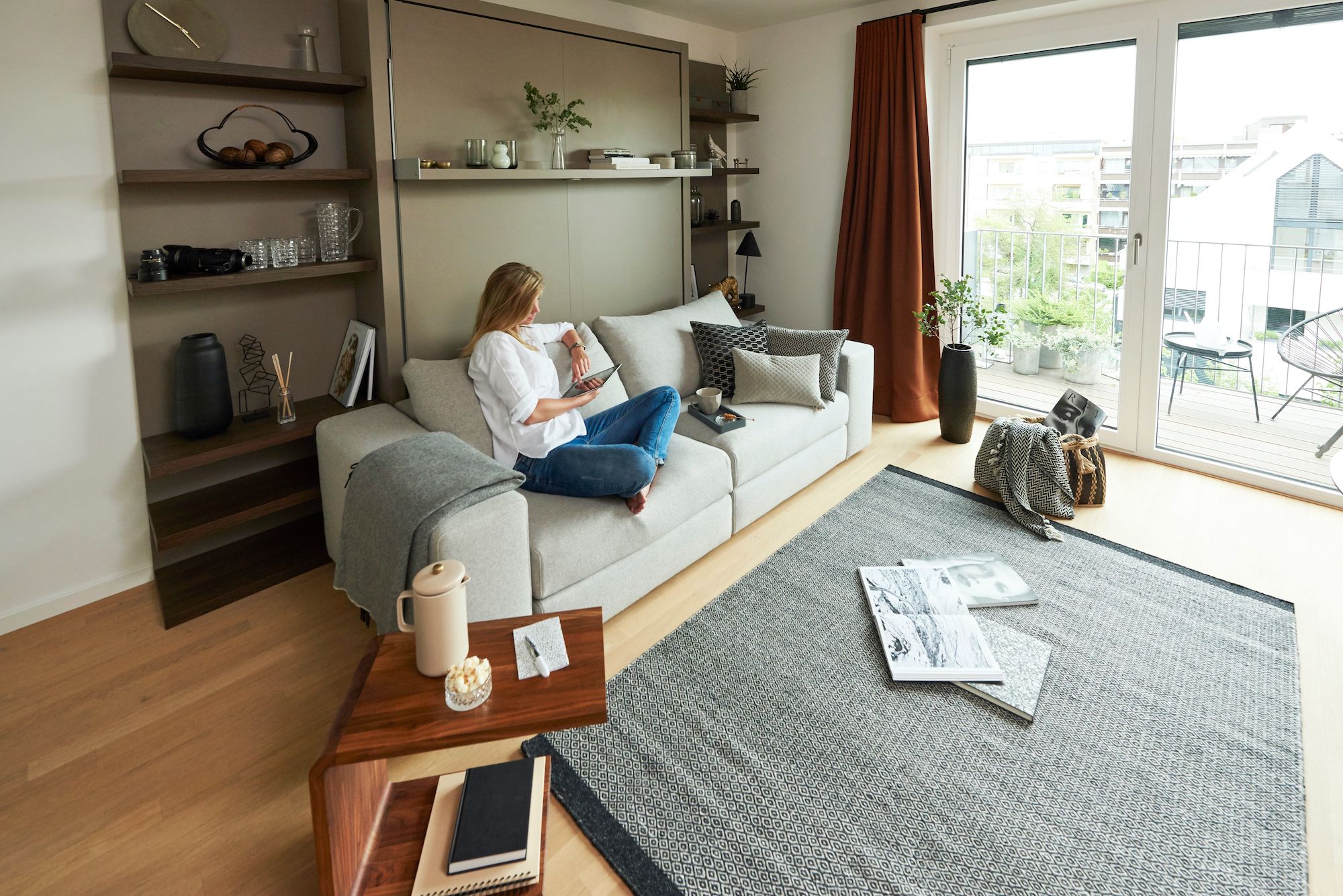 Frau mit elektronischem Tablet sitzt auf Couch in hellem Wohnzimmer