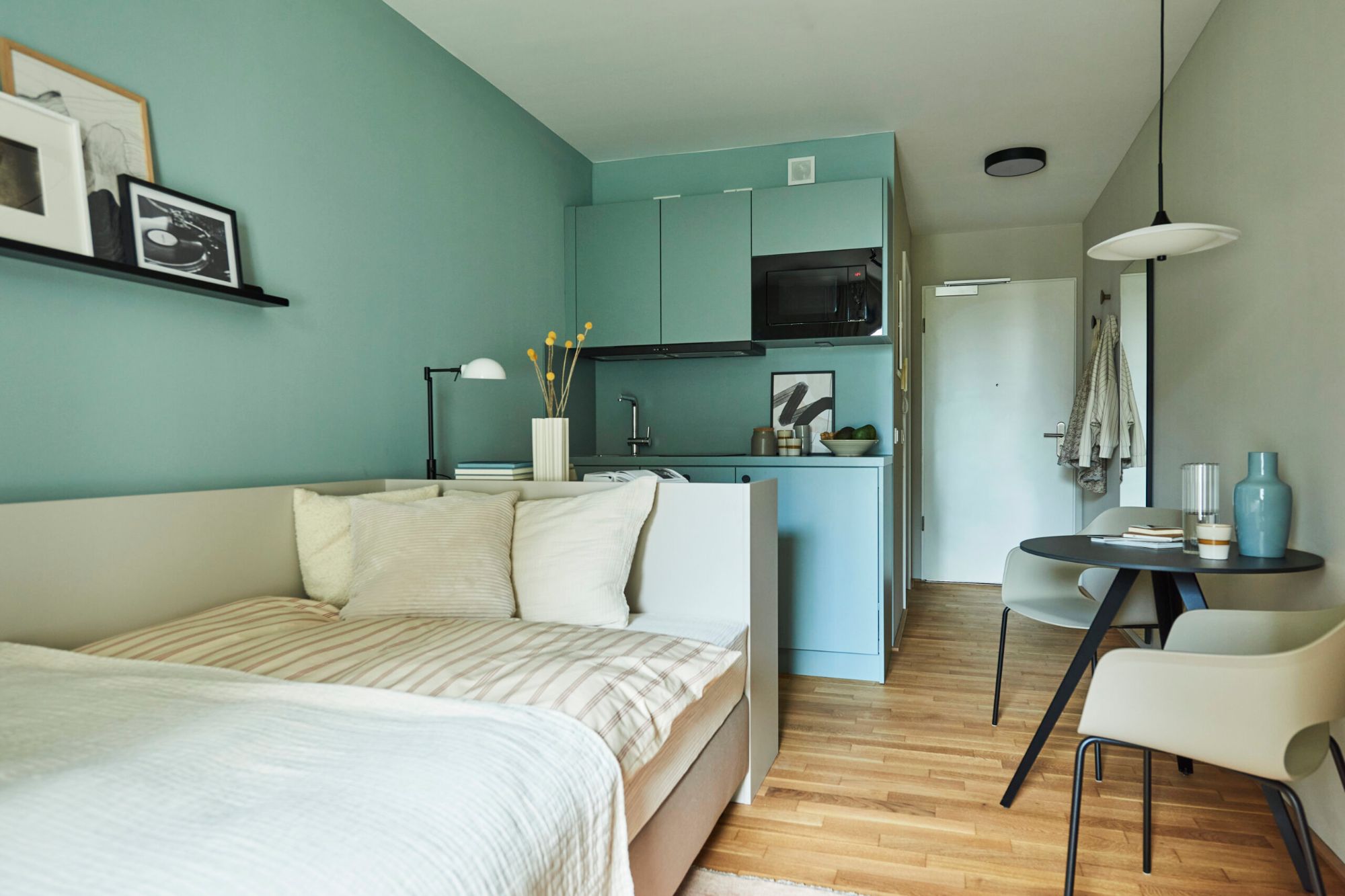 Zu sehen ist ein Apartment im Little East Frankfurt mit Bett, einer Küchenzeile sowie einem kleinen Tisch mit zwei Stühlen.