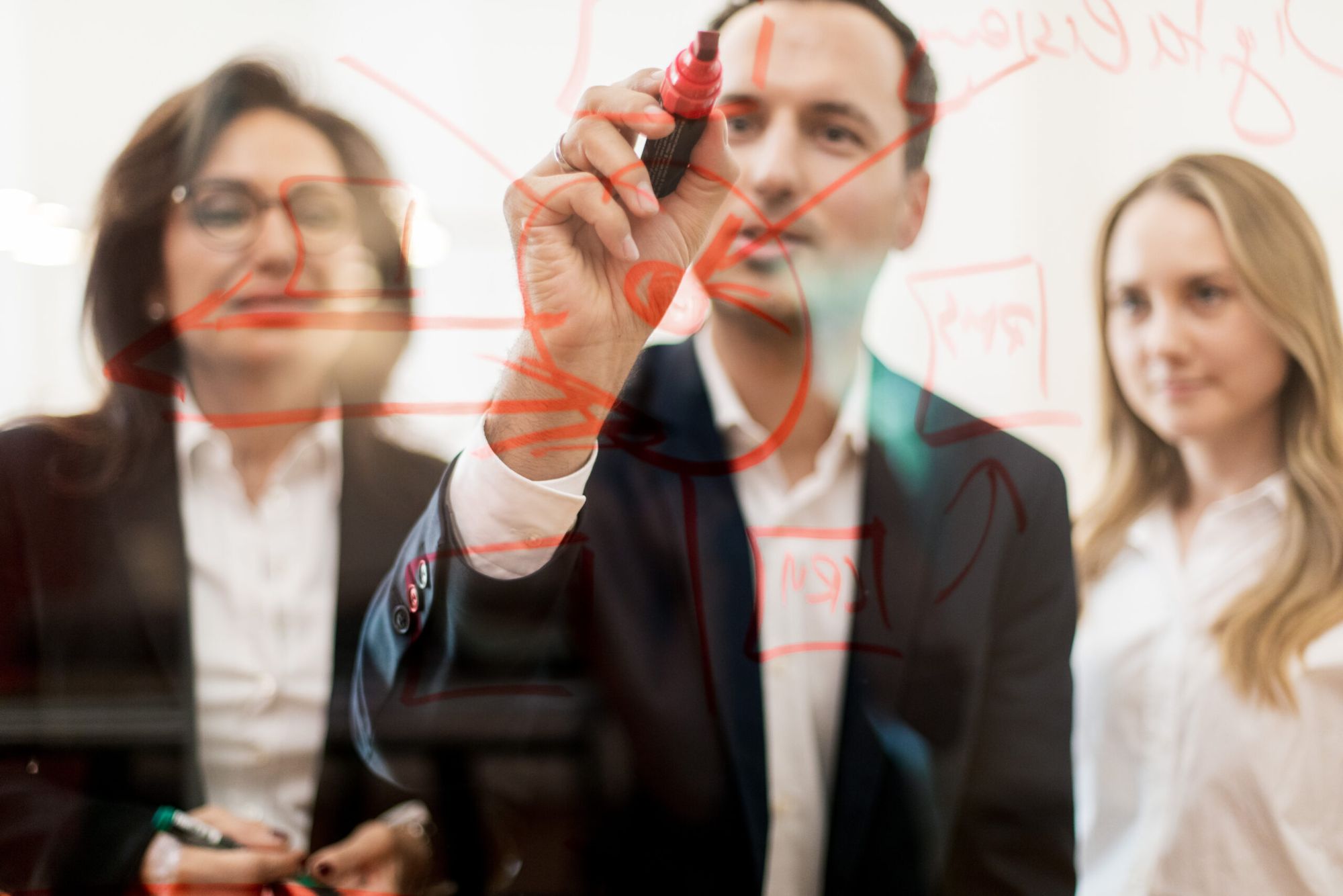 Team im Workshop hinter einer Glaswand, ein Mann skizziert mit rotem Marker